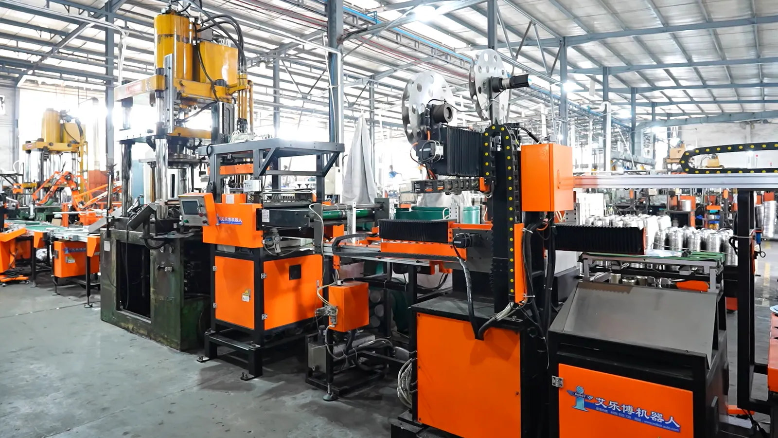 Orange automated press cells with transfer rails and a strip of stainless coil feeding the line in a cookware factory