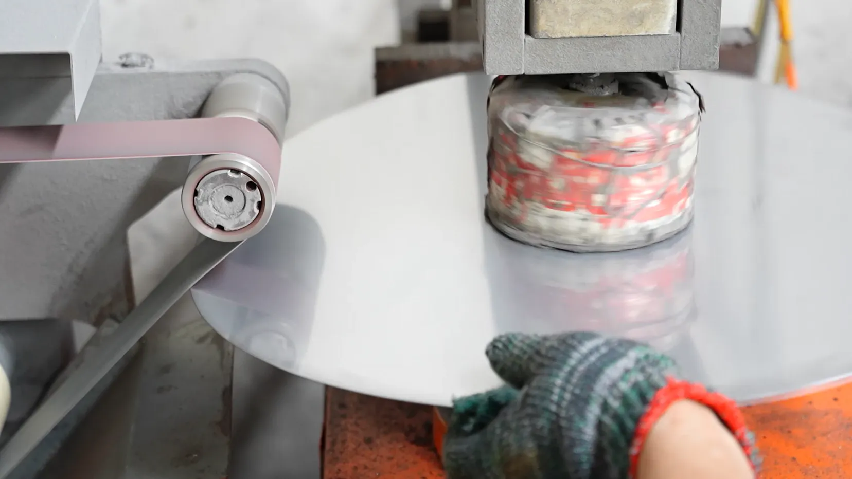 Operator hand-polishing a stainless steel blank on a belt — the finishing step that decides how a sample looks and lasts