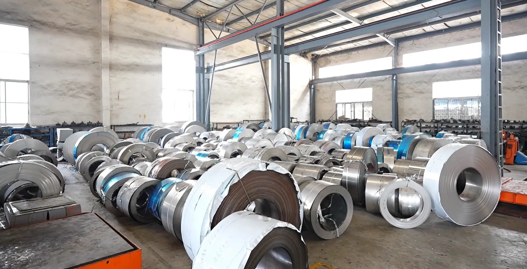 Stainless steel coil racks in a factory raw-material store — raw material is the largest cost line in a cookware quote