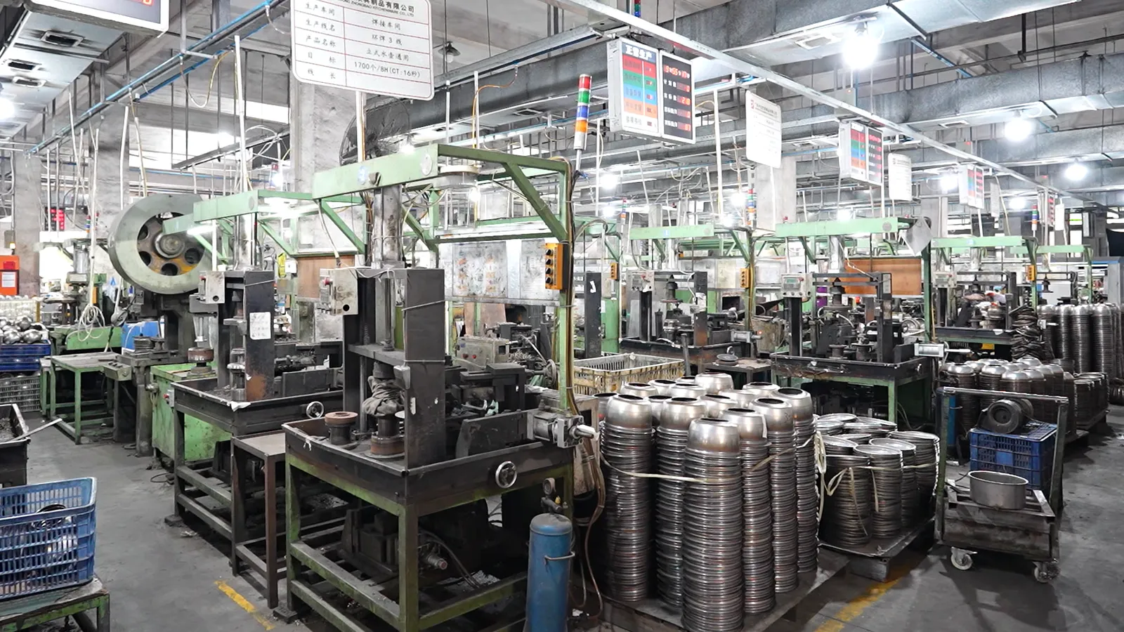 Stainless steel pot bodies stacked on trolleys between rows of presses in a cookware press shop