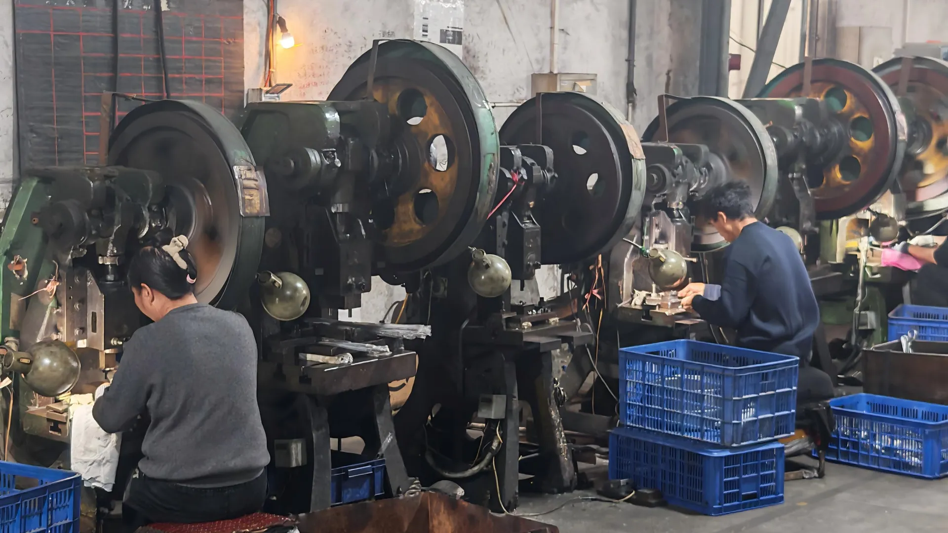 Operators at flywheel presses inside a stainless steel cookware factory stamping shop