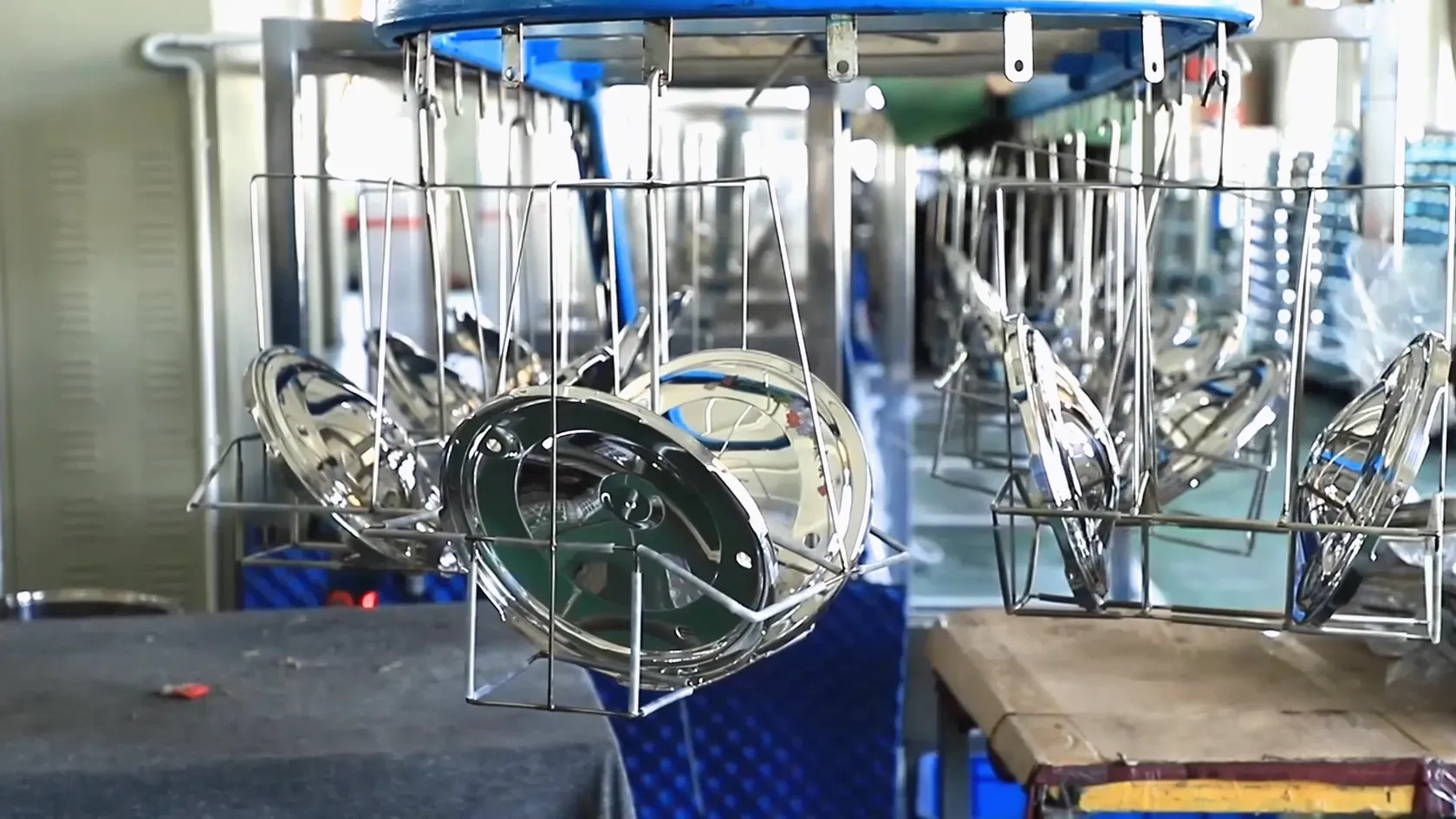 Rows of stainless steel pressure cooker lids hanging on wire fixtures along a finishing line in a cookware factory