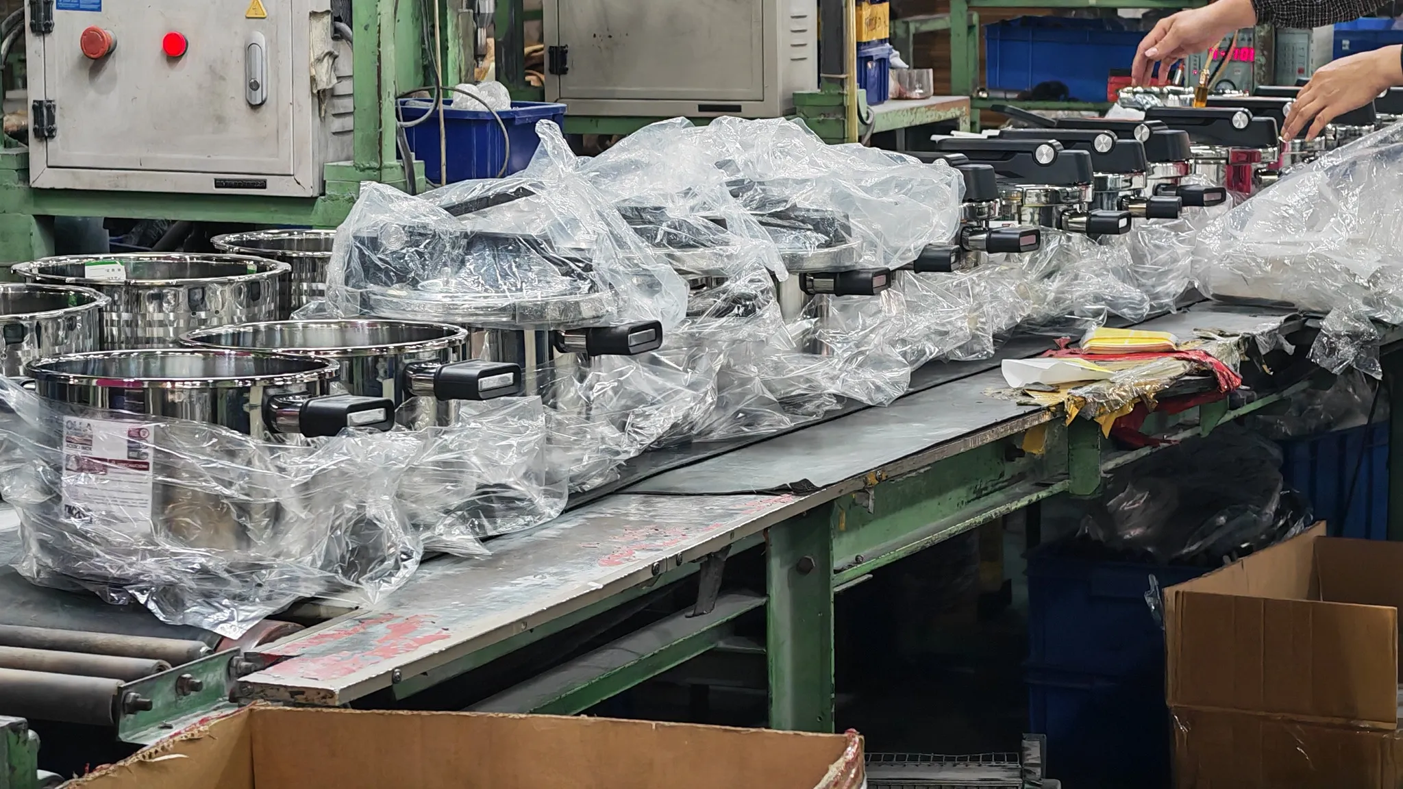 Bagged stainless steel cookware moving along a packing belt beside open corrugated cartons