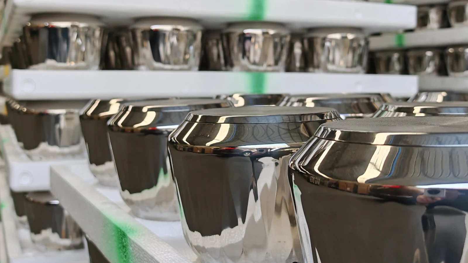 Rows of mirror-polished stainless steel pot bodies standing on white foam racks after finishing in a cookware plant
