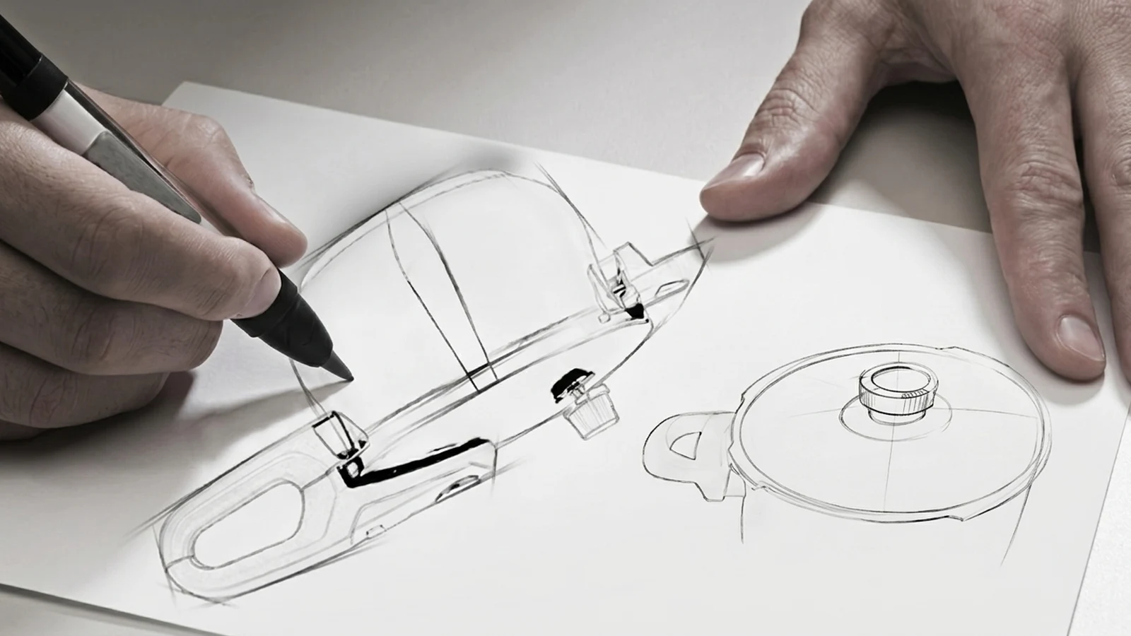 A hand drawing a technical sketch of a stainless steel cookware body and a lid, in a studio setting