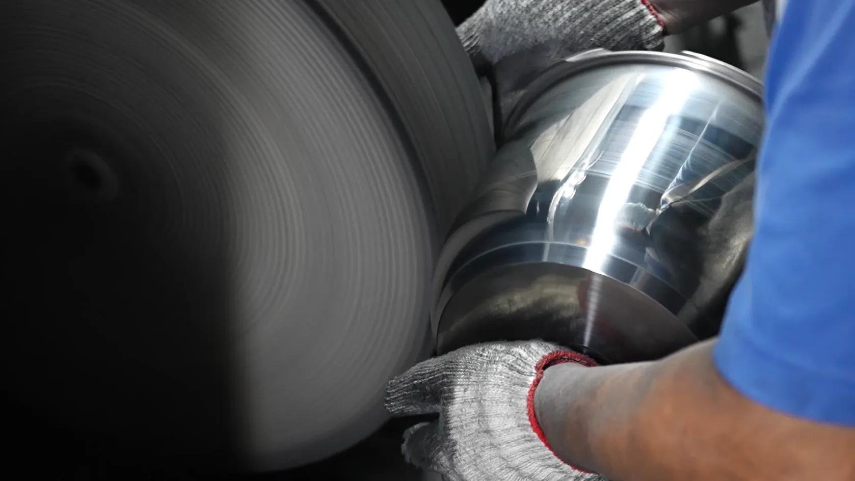 Factory operator polishing a stainless steel pot body on a belt in the Potobelo workshop; polishing changes the surface, not the alloy family