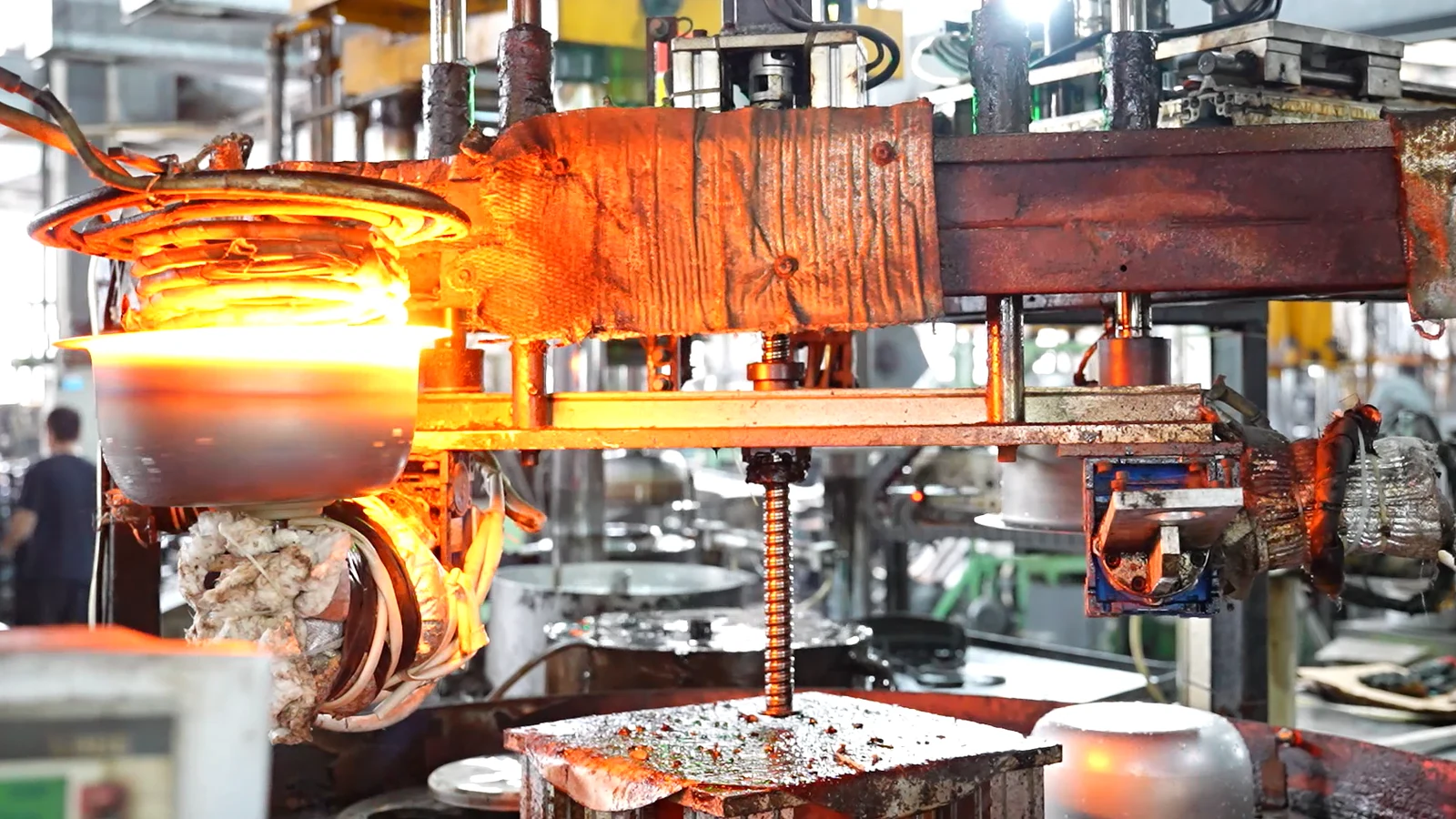 A stainless steel workpiece glowing orange under an induction heating coil at a station in a cookware factory