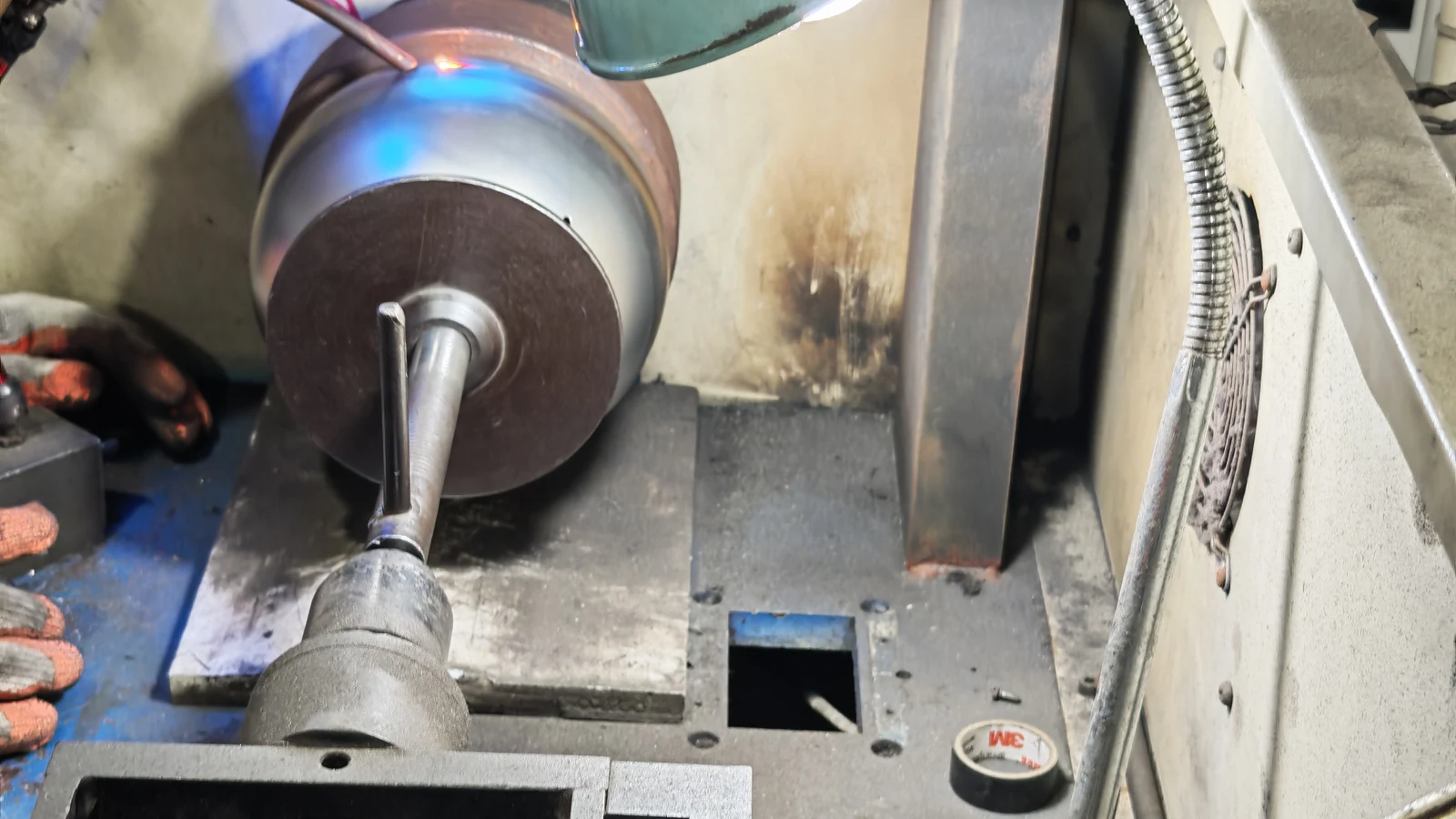A stainless steel pot body mounted on the spindle of a forming station, with the tool pressed against the wall during a shaping pass