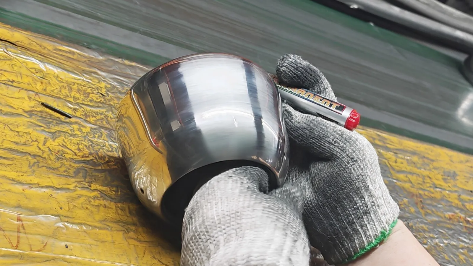 A gloved operator holding a polished stainless steel kettle body on the finishing line