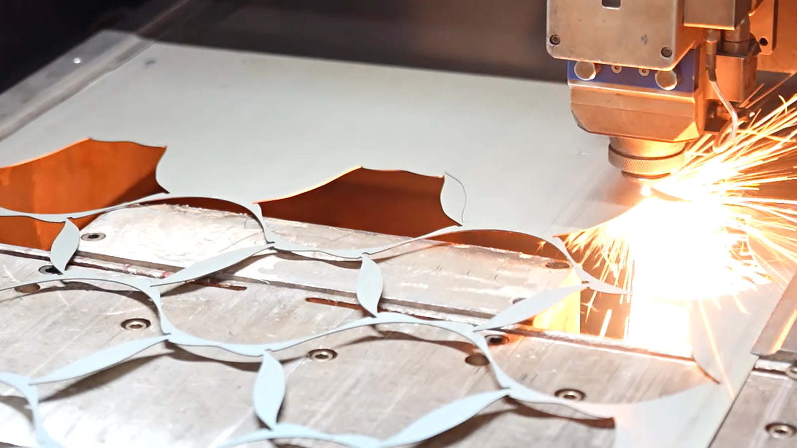 A laser head cutting nested profiled blanks from a sheet of stainless steel, with sparks at the cut line