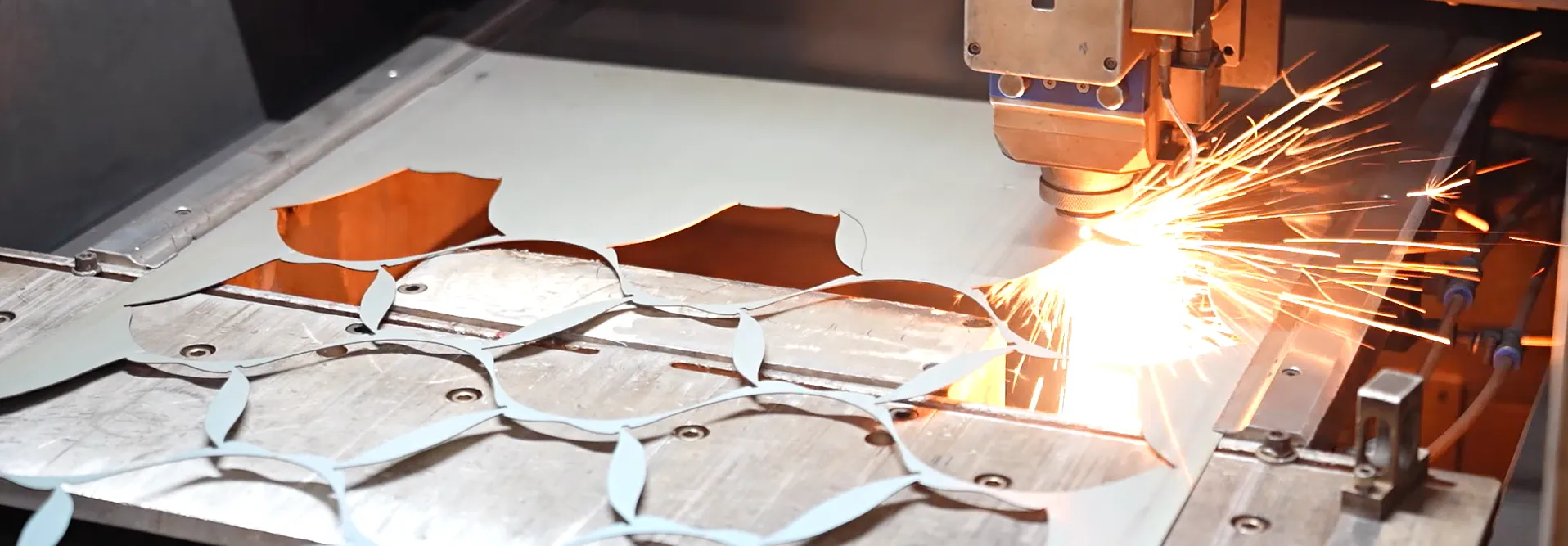 Laser cutting stainless steel sheet with sparks inside a factory, an in-house process step that separates manufacturers from traders