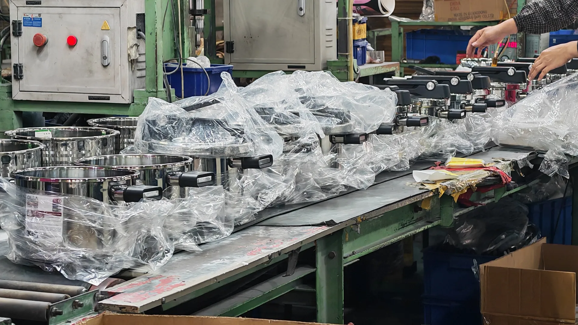 Finished stainless steel pots being bagged on a factory packing bench before export cartons are sealed