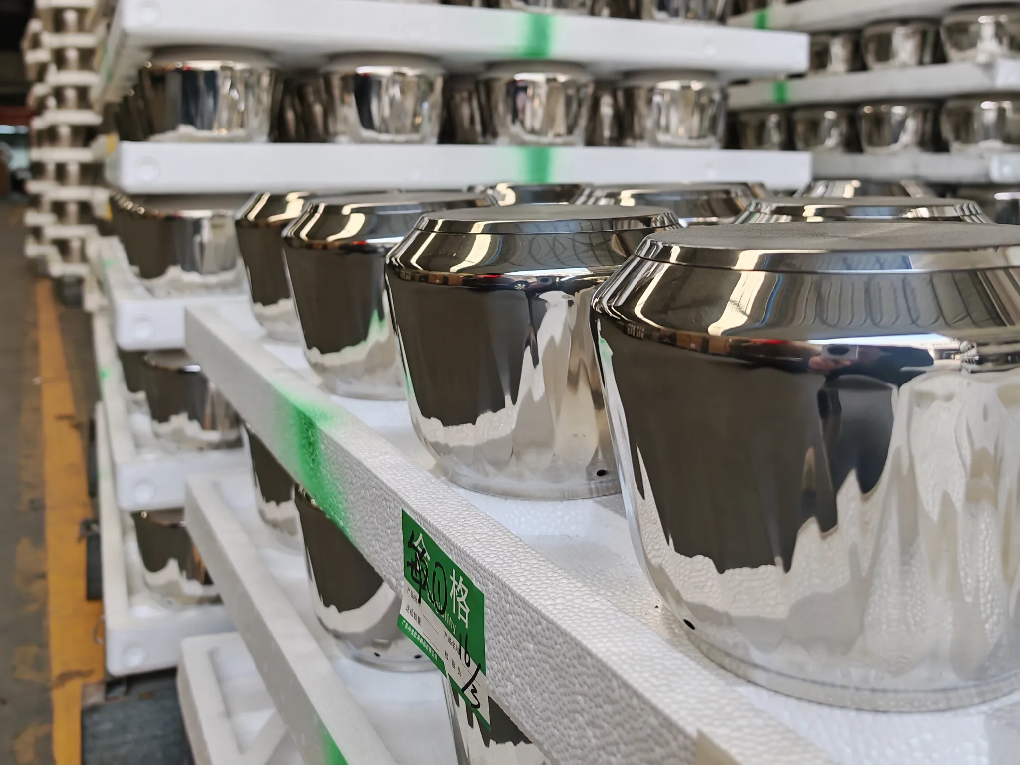 Mirror-polished stainless steel pot bodies staged on racks with green QC labels in the Potobelo finishing shop, waiting for batch inspection