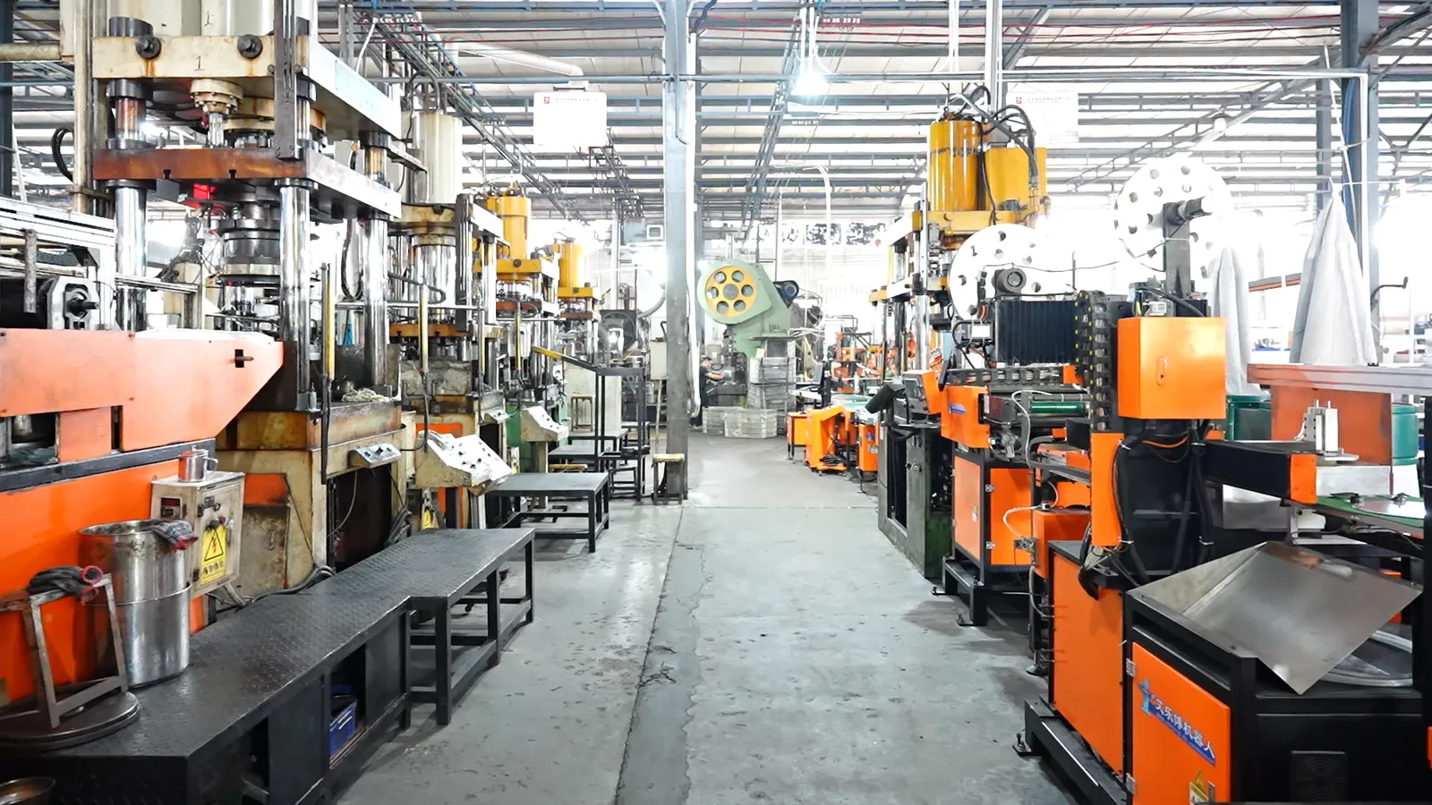 Rows of hydraulic presses on both sides of the central aisle of a cookware press hall, with a steel coil on a decoiler between the lines