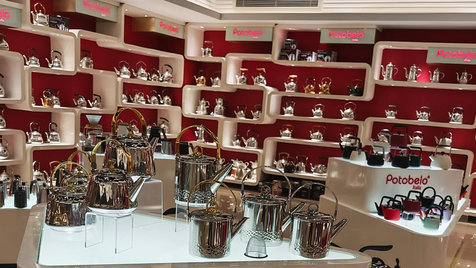 Potobelo showroom display wall with hundreds of stainless steel kettles and pots arranged in illuminated white cubbies under red panels