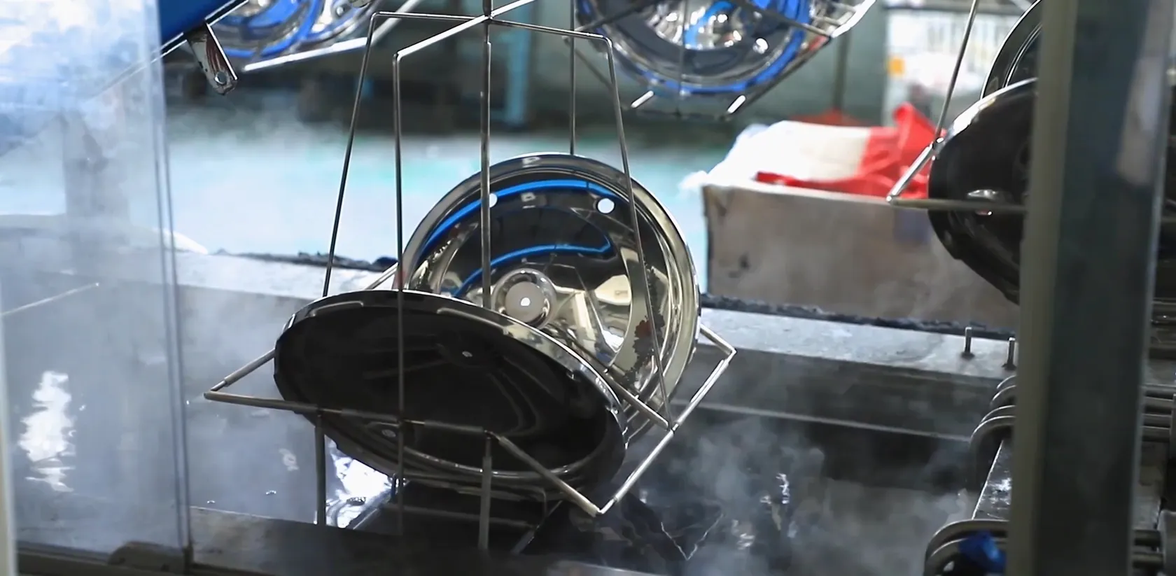Wire fixtures carrying stainless steel parts out of a steaming treatment bath on a finishing line