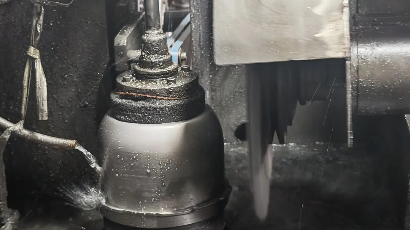 A stainless steel vessel held on a forming machine during a production operation, with metal chips around it
