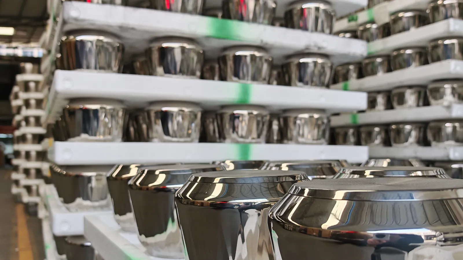 Mirror-polished pot bodies stacked in layers on white rack shelves in a factory, waiting between production stages